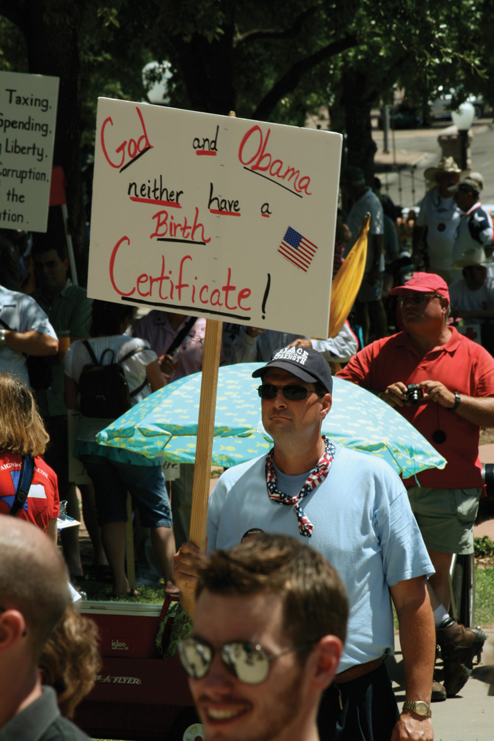 Photo of Tea Party supporters at a rally. One man holds a sign that reads, "God and Obama—neither have a birth certificate!"
