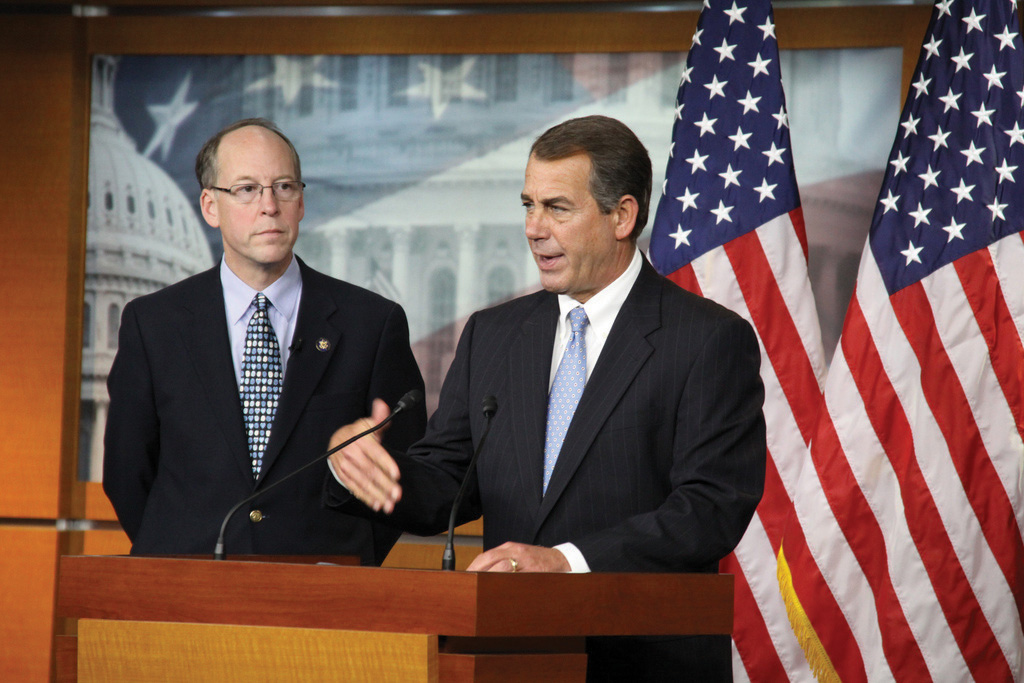 Photo of Leader Boehner (R-OH) standing next to Greg Walden (R-OR). Both are behind a podium. Two large American flags in the background.