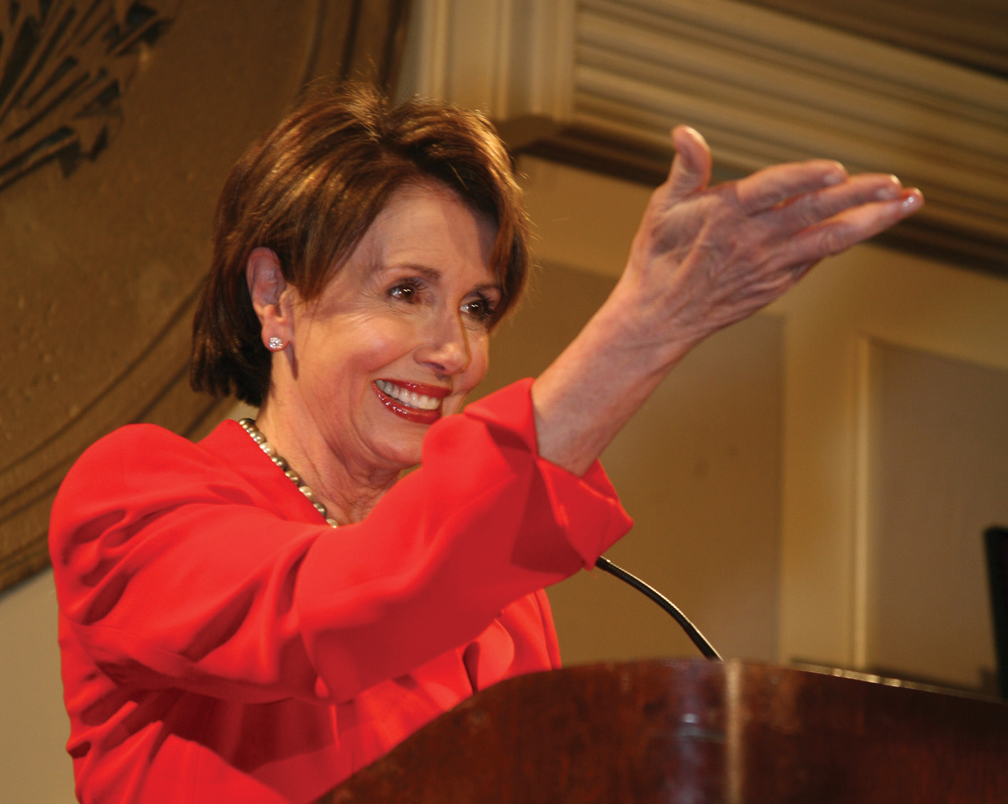 Photo of Nancy Pelosi standing behind a podium, smiling