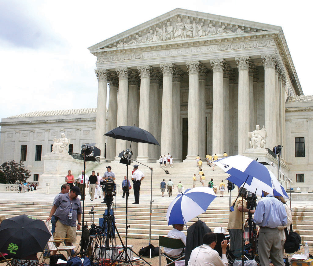 Front-facing photo of the Supreme Court building and plaza with many journalists and photographers in the foreground